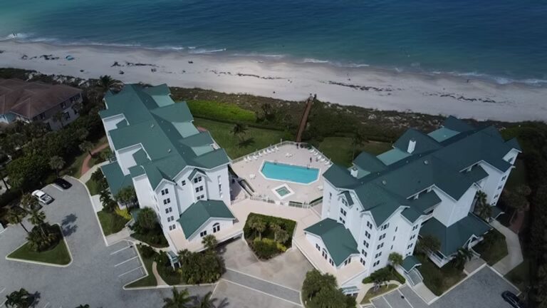 The Gables of Vero Beach Aerial view of a coastal resort with a pool, next to a sandy beach with waves.